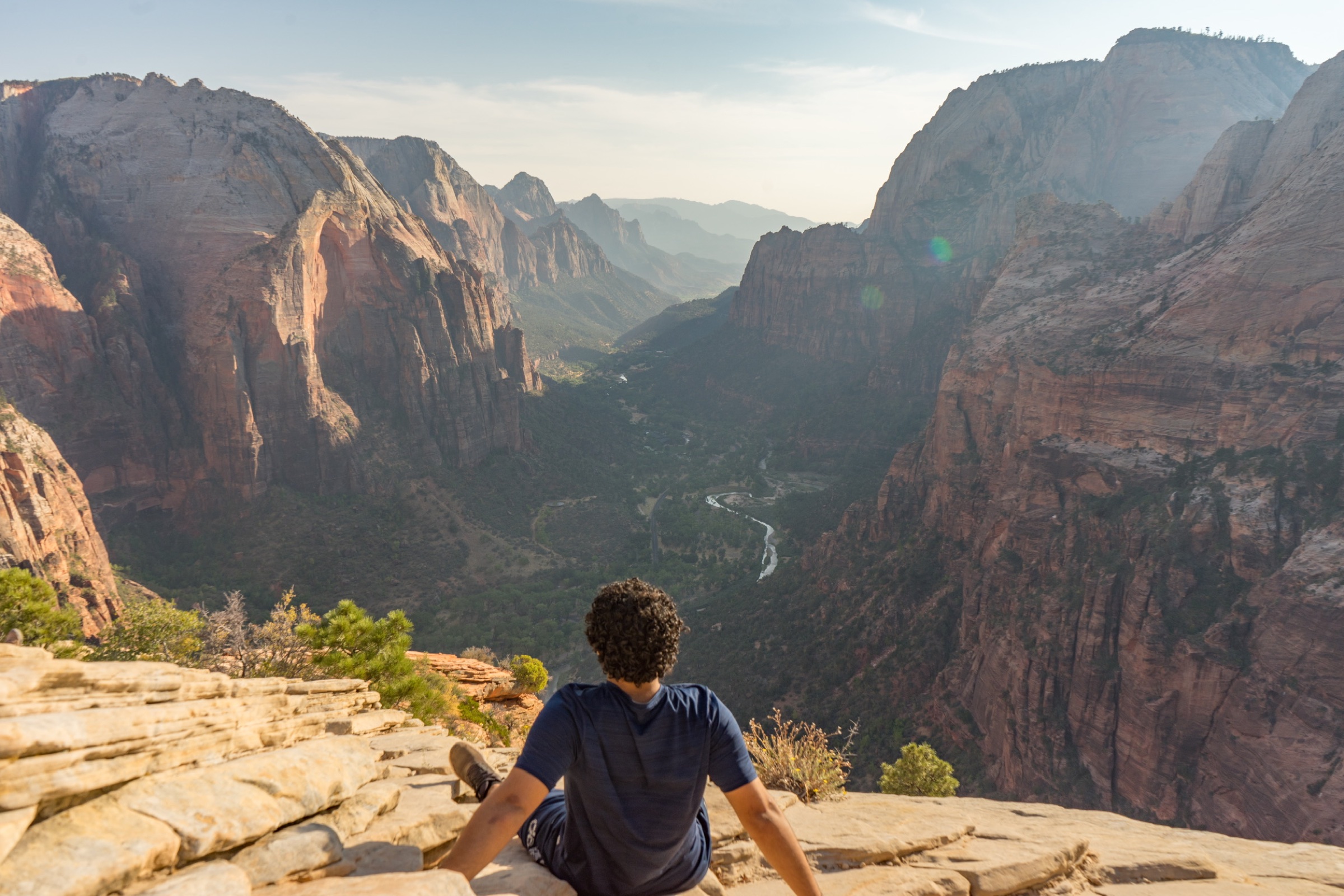 A person seated above a deep red-rock canyon valley
