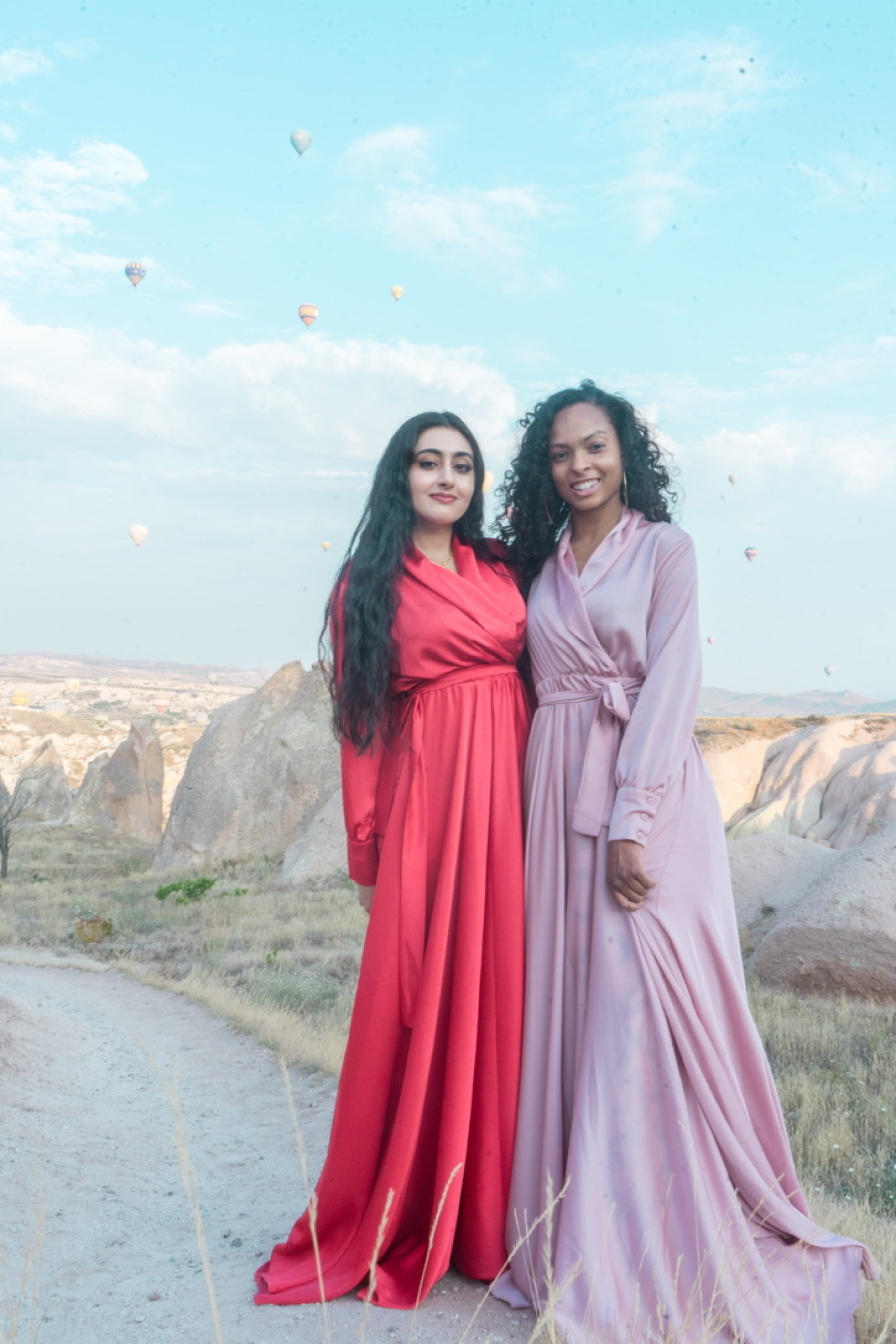 Two women in flowing dresses with hot air balloons behind them
