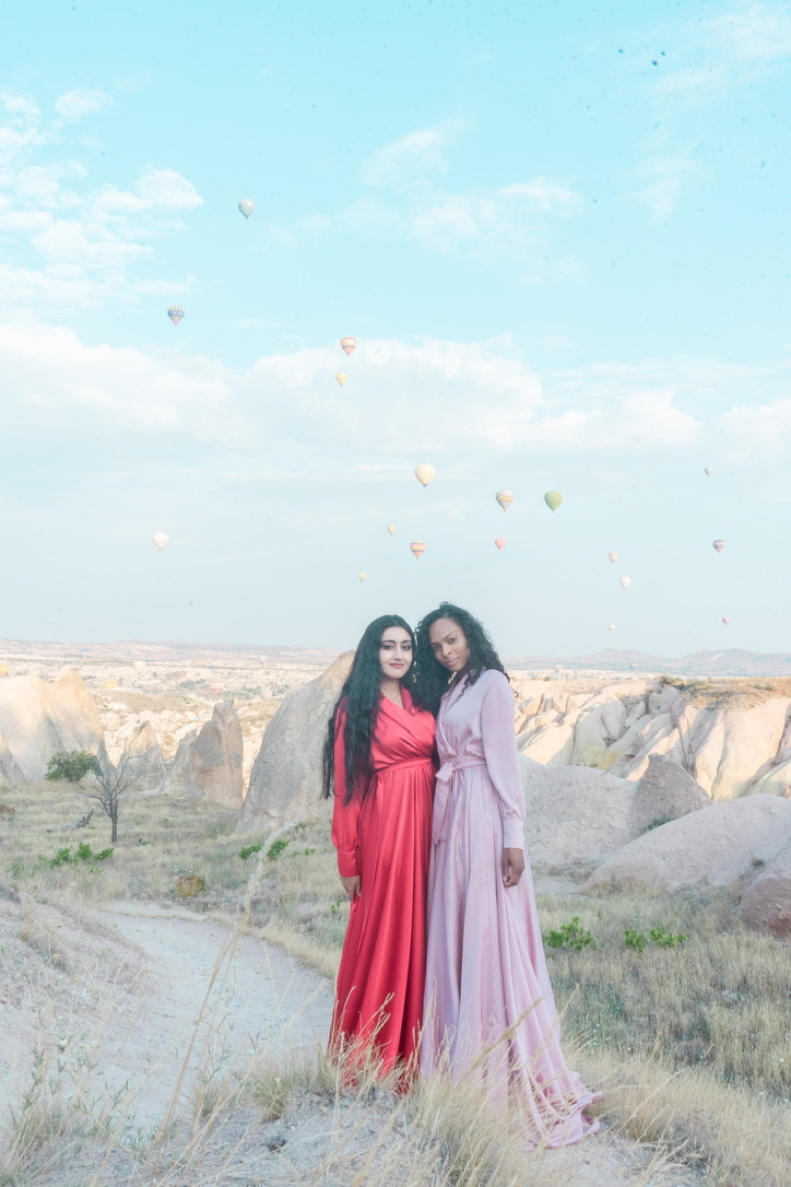 Two women in red and pink gowns beneath hot air balloons
