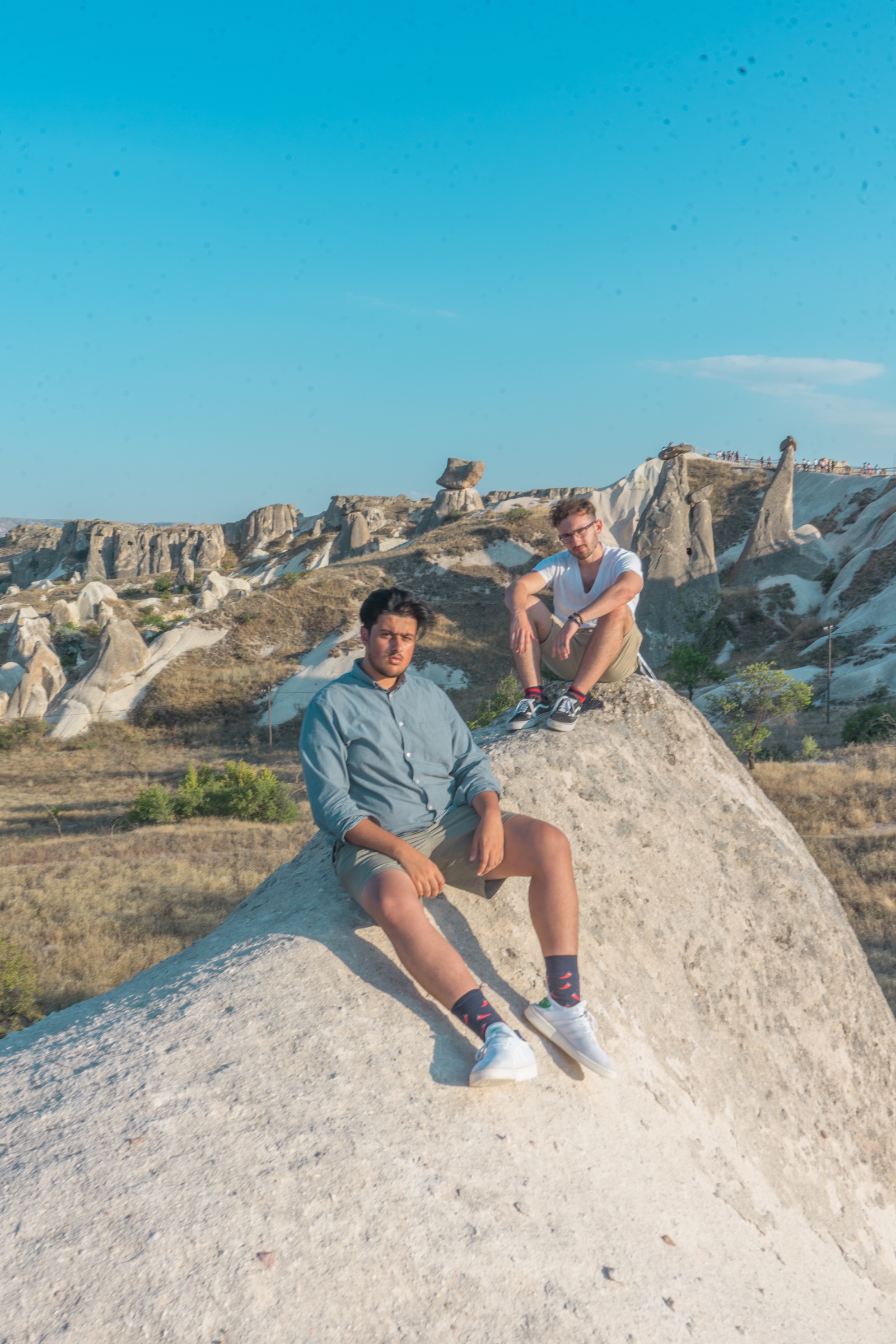 Two friends seated on a pale rock formation beneath a blue sky