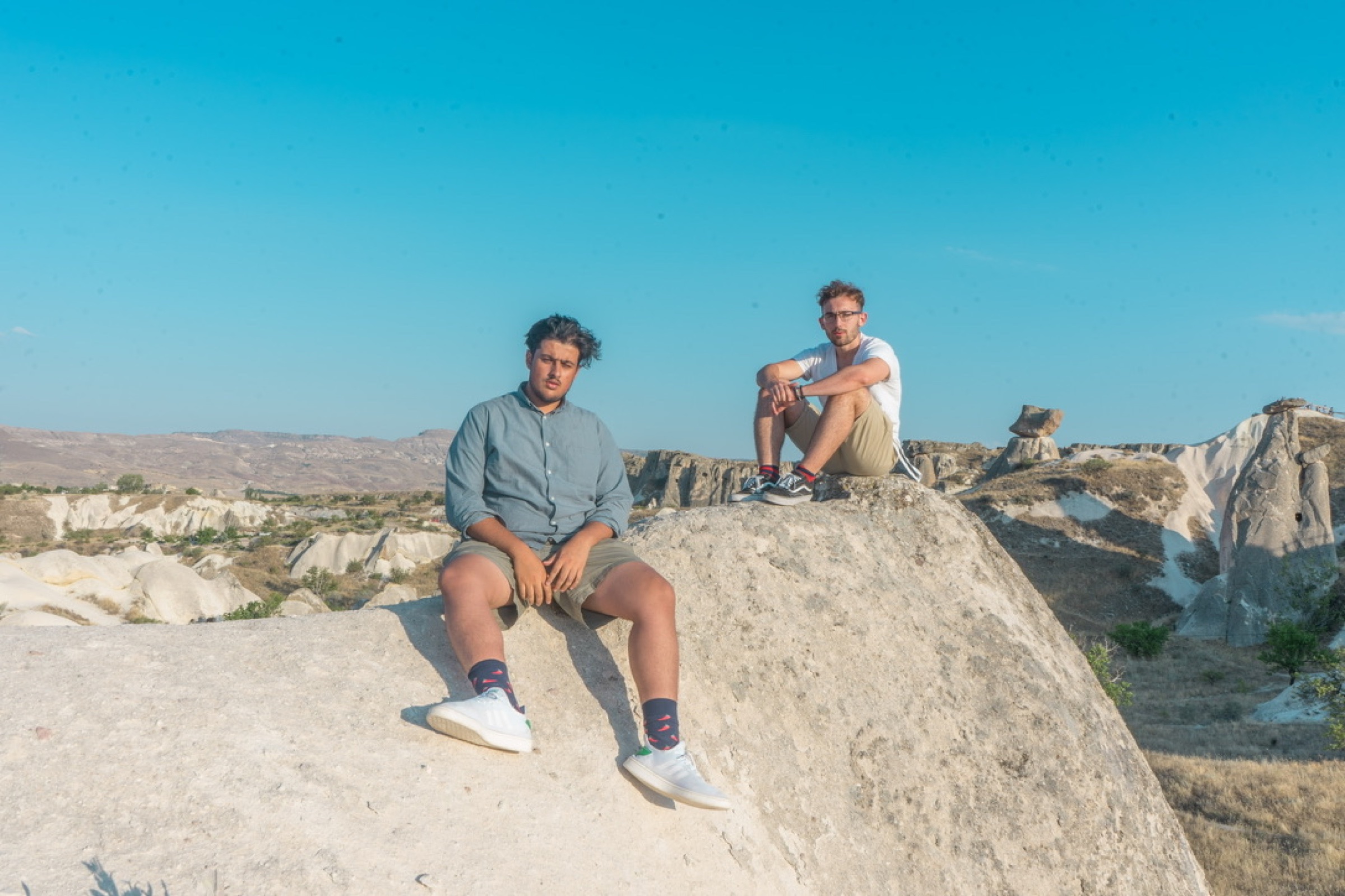 Two friends seated on a pale rock formation beneath a blue sky