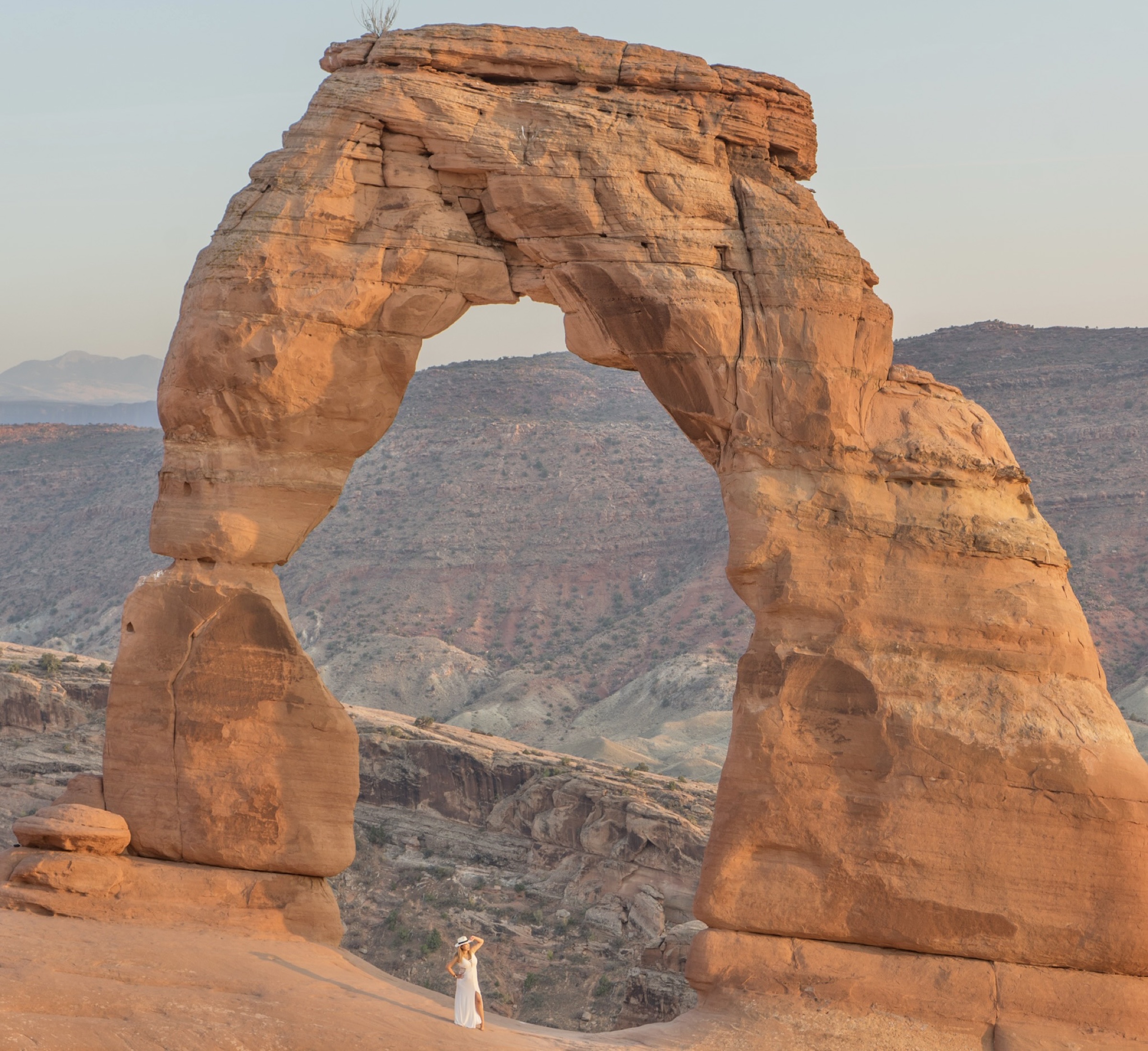 A person in a white dress standing beneath Delicate Arch