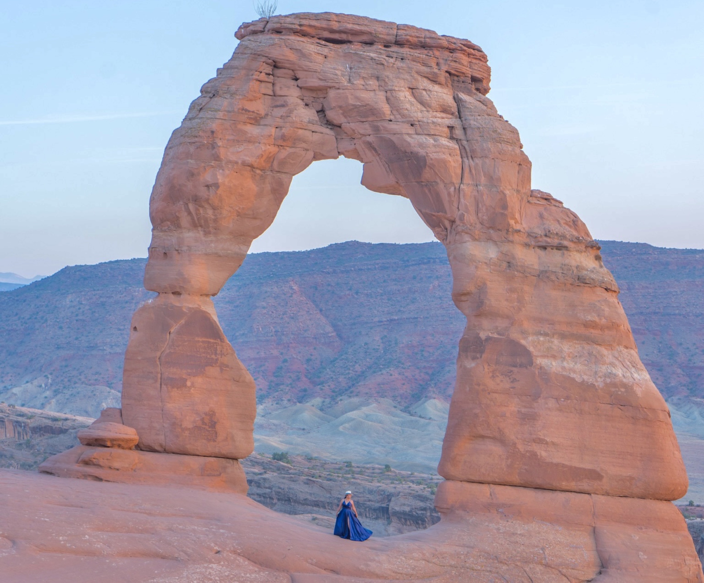 A person in a blue dress standing beneath Delicate Arch