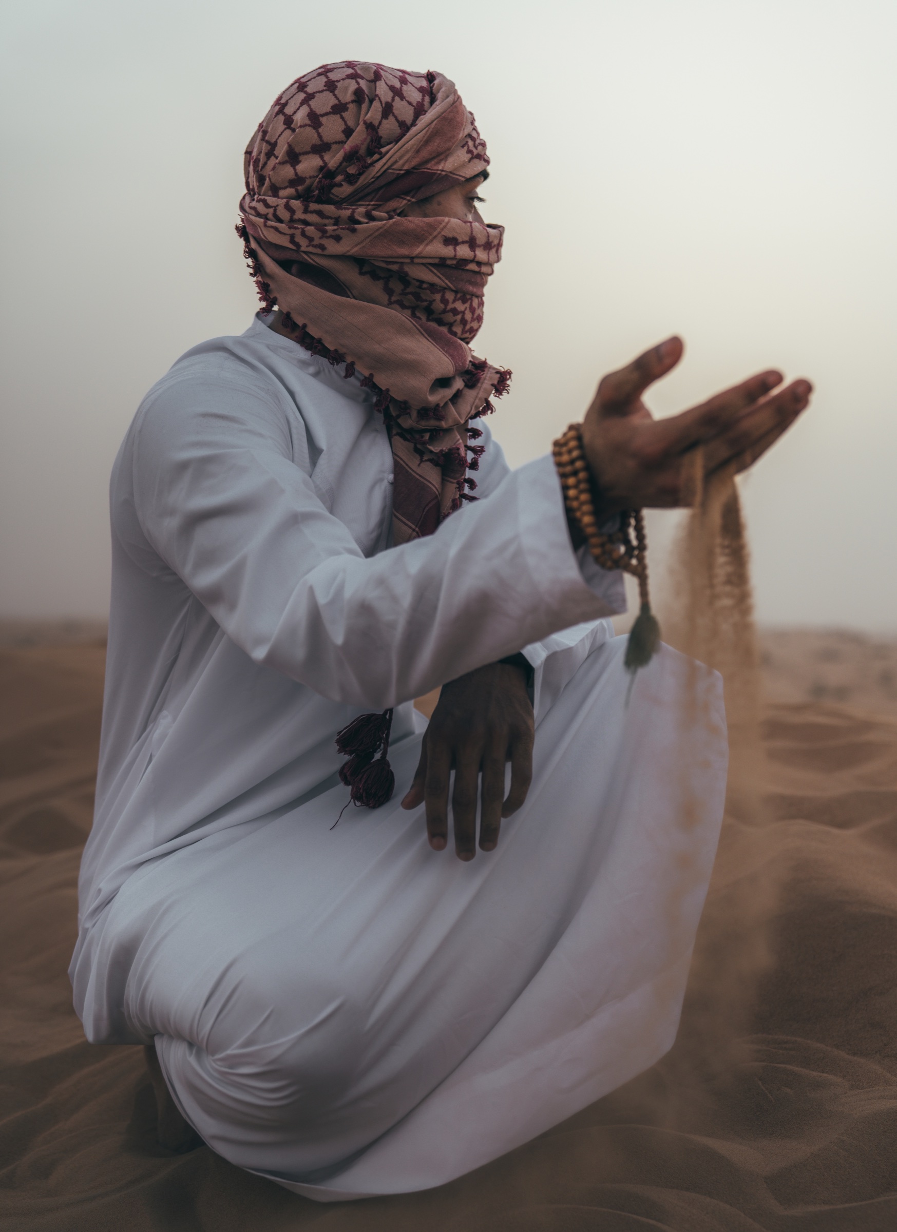 A seated person in white clothing and a wrapped scarf in the desert