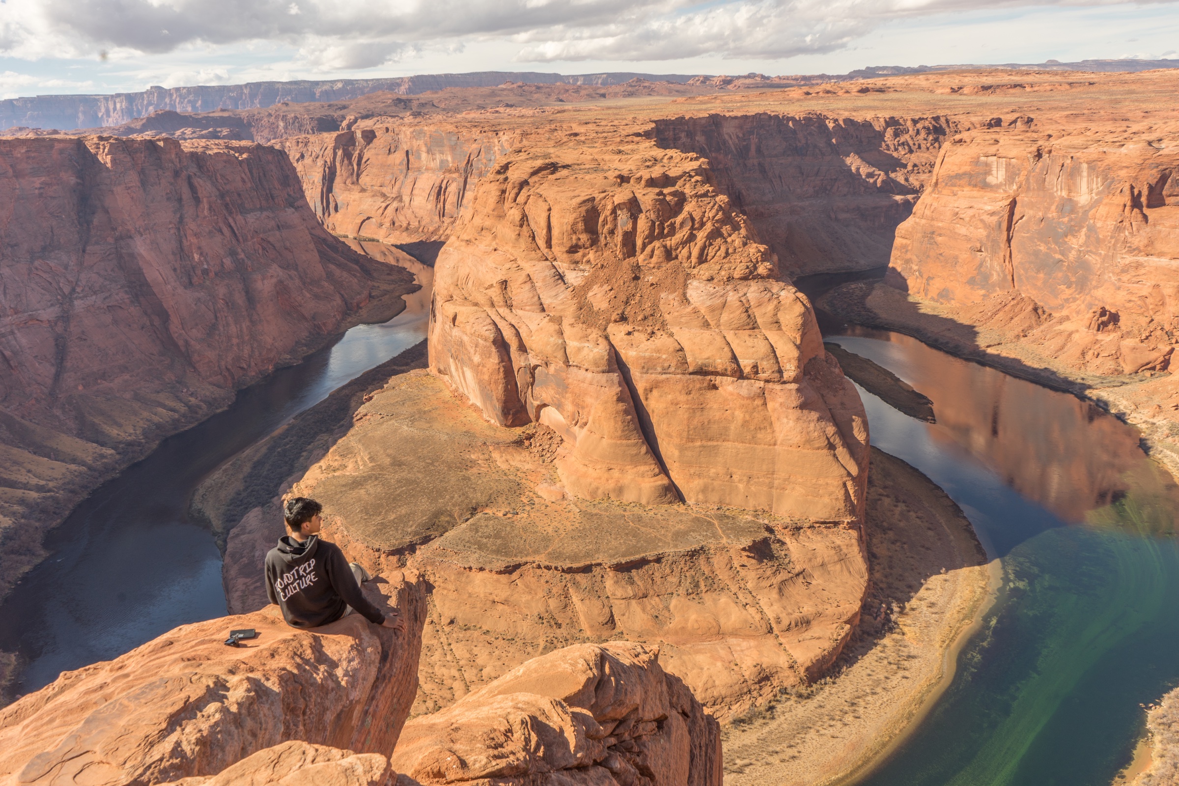 A person seated above a winding river surrounded by red canyon walls