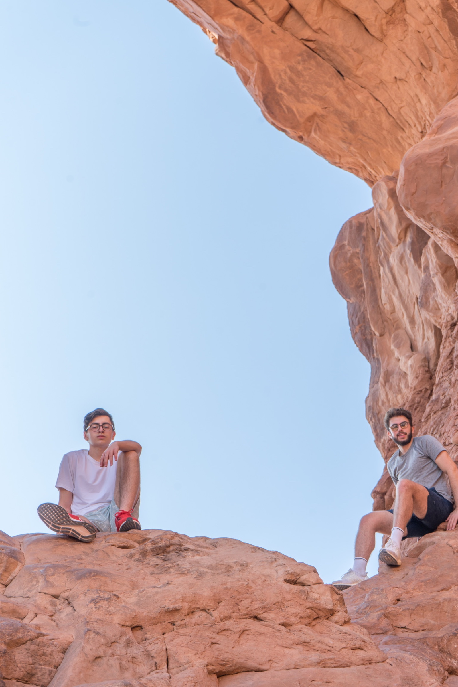 Two friends seated on red rocks beneath a clear blue sky