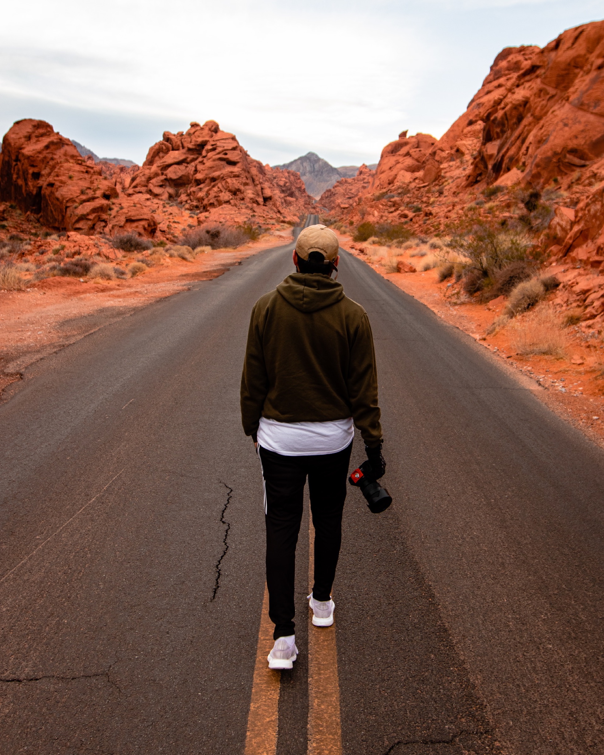 A photographer walking down a road surrounded by red rock formations